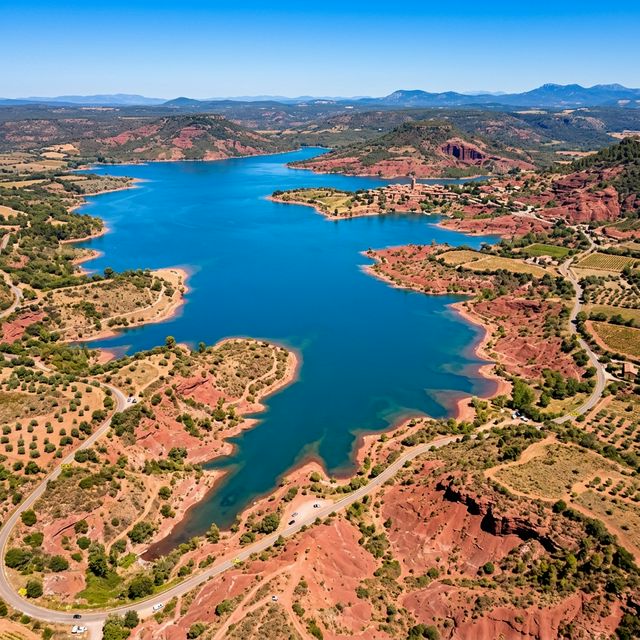 Vue aérienne du lac du Salagou, eaux bleues profondes entourées de terres rouge vif de ruffe sous le soleil méditerranéen